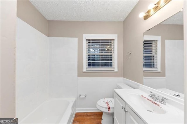 bathroom featuring a textured ceiling, wood finished floors, vanity, and a bathtub