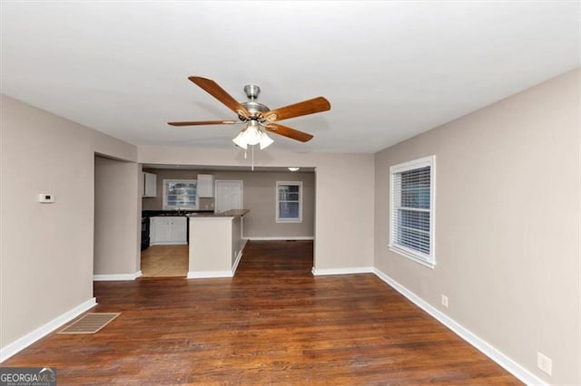 unfurnished living room with a ceiling fan, visible vents, dark wood finished floors, and baseboards