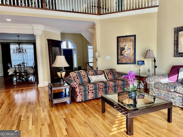 living area featuring a chandelier, a high ceiling, wood finished floors, ornate columns, and crown molding