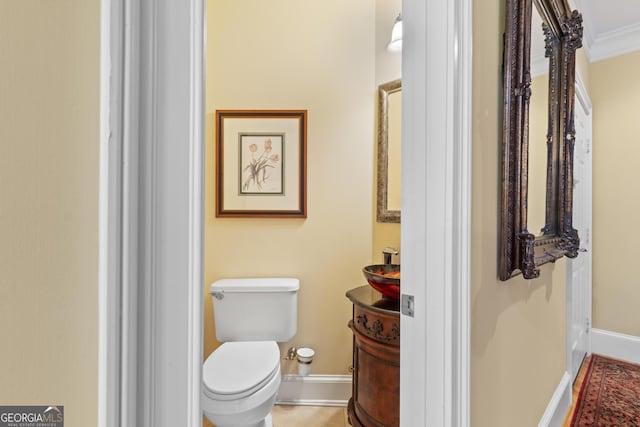 half bathroom with toilet, baseboards, and ornamental molding