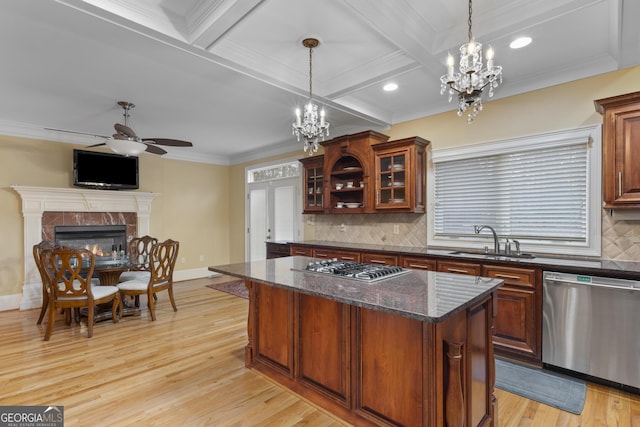 kitchen with light wood finished floors, a tiled fireplace, appliances with stainless steel finishes, a sink, and beamed ceiling