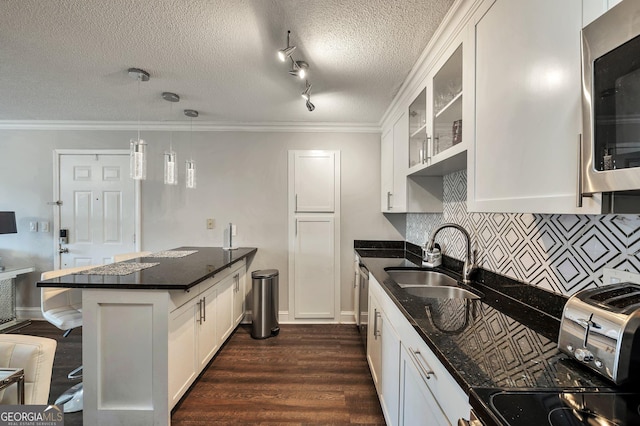 kitchen featuring a sink, white cabinetry, hanging light fixtures, stainless steel microwave, and glass insert cabinets