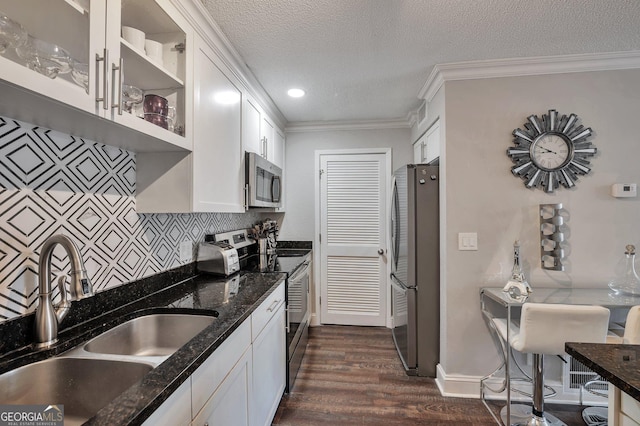 kitchen with dark stone counters, appliances with stainless steel finishes, a sink, and white cabinets