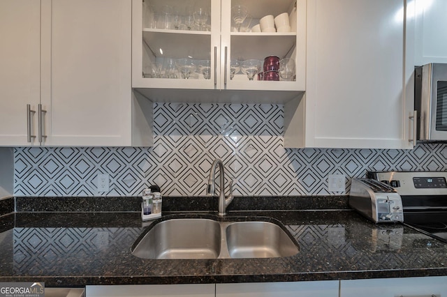 kitchen with glass insert cabinets, dark stone counters, white cabinets, and a sink