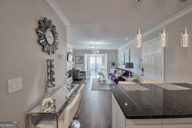 kitchen featuring dark wood finished floors, open floor plan, dark stone countertops, crown molding, and pendant lighting