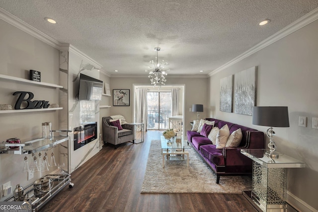 living area with a chandelier, a textured ceiling, dark wood-style flooring, ornamental molding, and a glass covered fireplace