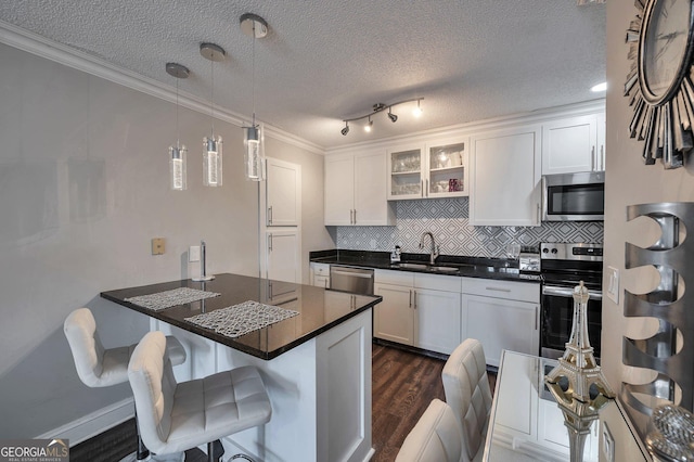 kitchen featuring stainless steel appliances, a sink, white cabinets, a kitchen bar, and glass insert cabinets