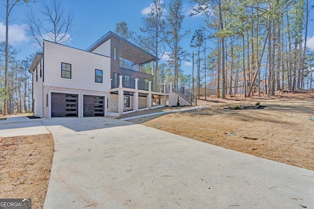 view of front facade with an attached garage, a balcony, stairs, driveway, and stucco siding