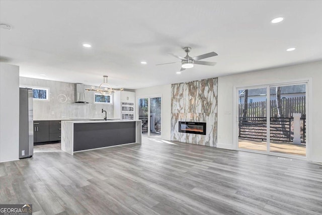 kitchen with an island with sink, wall chimney exhaust hood, freestanding refrigerator, light countertops, and a fireplace