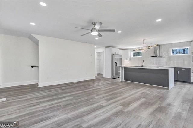 kitchen featuring light wood-style flooring, light countertops, hanging light fixtures, stainless steel refrigerator with ice dispenser, and wall chimney exhaust hood