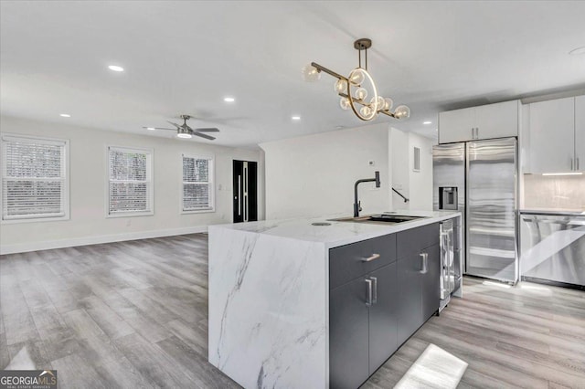 kitchen with decorative light fixtures, stainless steel appliances, white cabinetry, a sink, and an island with sink