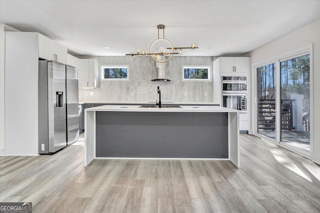 kitchen featuring white cabinets, an island with sink, stainless steel appliances, light countertops, and pendant lighting