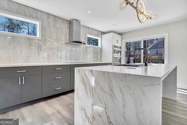 kitchen featuring a spacious island, decorative light fixtures, gray cabinets, light wood-type flooring, and wall chimney range hood