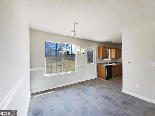 kitchen featuring pendant lighting, brown cabinets, a notable chandelier, light countertops, and a sink