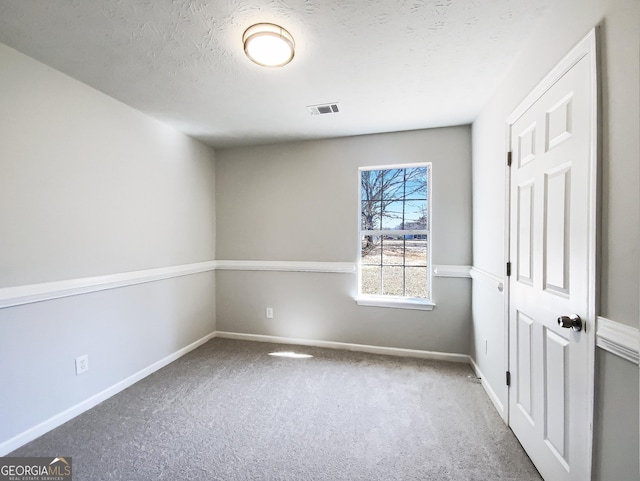 carpeted empty room featuring baseboards, visible vents, and a textured ceiling