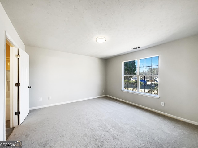 carpeted spare room featuring visible vents, baseboards, and a textured ceiling