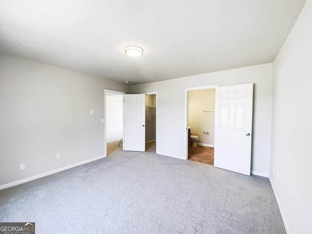 unfurnished bedroom featuring ensuite bathroom, a walk in closet, light colored carpet, and baseboards