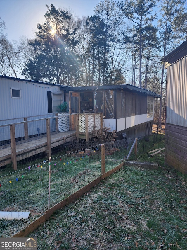 back of property featuring a deck, a lawn, and a sunroom