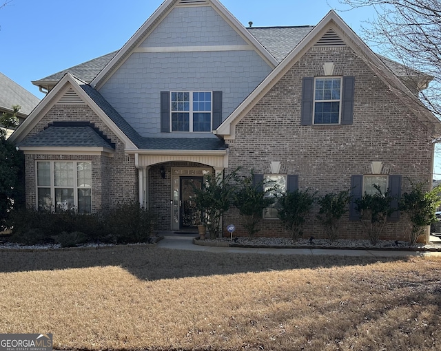 view of front of house with brick siding, roof with shingles, and a front yard