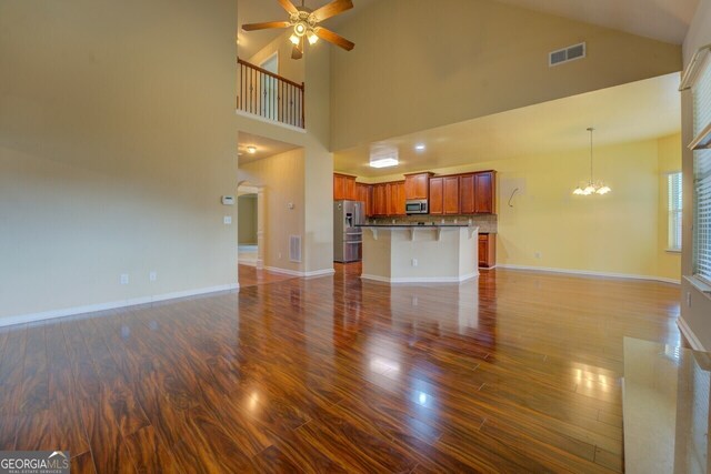 1186 Diamond Xing, Mcdonough, GA 30252 - unfurnished living room featuring dark wood-type flooring, ceiling fan, a chandelier, high vaulted ceiling, and baseboards
