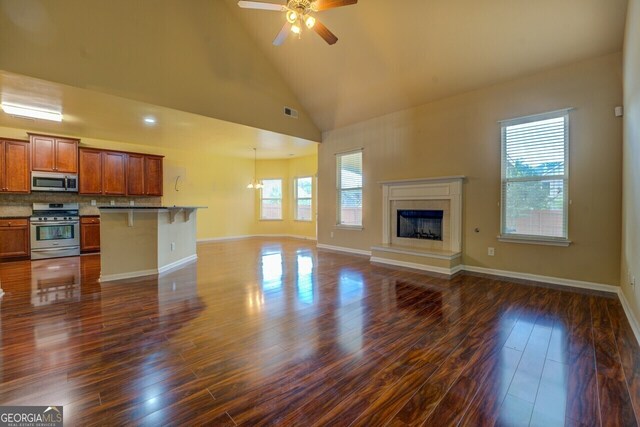 1186 Diamond Xing, Mcdonough, GA 30252 - unfurnished living room featuring dark wood-style flooring, ceiling fan, a fireplace, baseboards, and high vaulted ceiling
