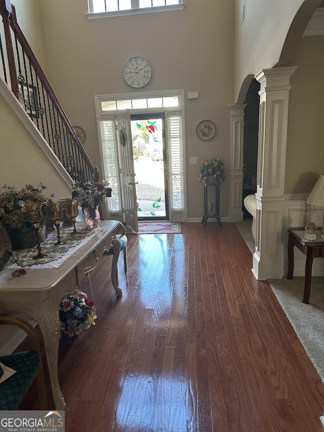 entryway with arched walkways, a towering ceiling, dark wood-style floors, stairway, and ornate columns