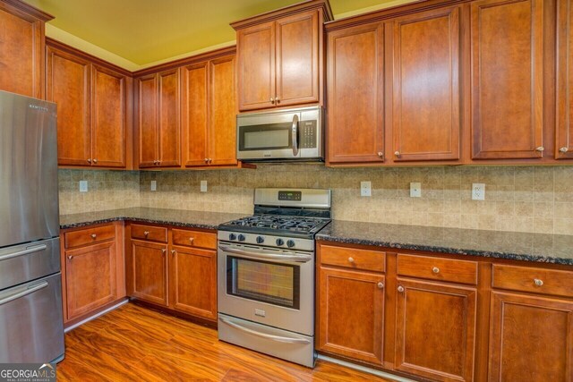 1186 Diamond Xing, Mcdonough, GA 30252 - kitchen featuring appliances with stainless steel finishes, wood finished floors, dark stone countertops, decorative backsplash, and brown cabinets