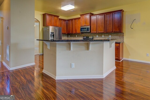 1186 Diamond Xing, Mcdonough, GA 30252 - kitchen featuring appliances with stainless steel finishes, dark wood finished floors, a breakfast bar, tasteful backsplash, and arched walkways
