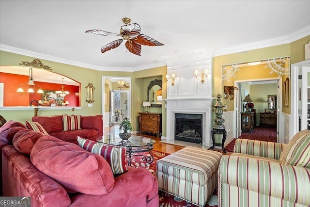 living area featuring ceiling fan with notable chandelier, ornamental molding, wood finished floors, and a fireplace with flush hearth