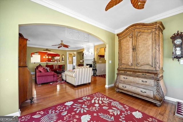 living area with ceiling fan, arched walkways, crown molding, and wood finished floors