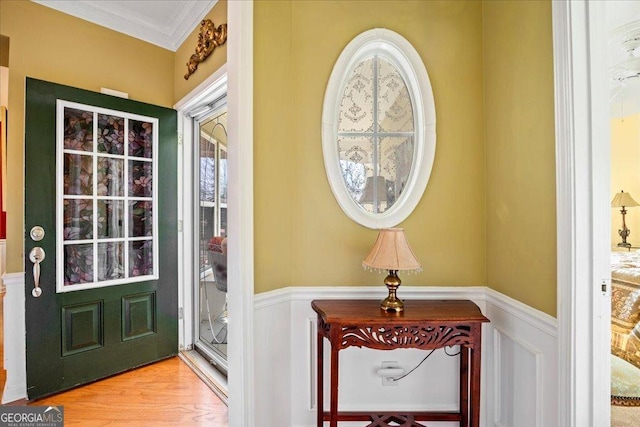 doorway to outside featuring wainscoting, wood finished floors, and crown molding