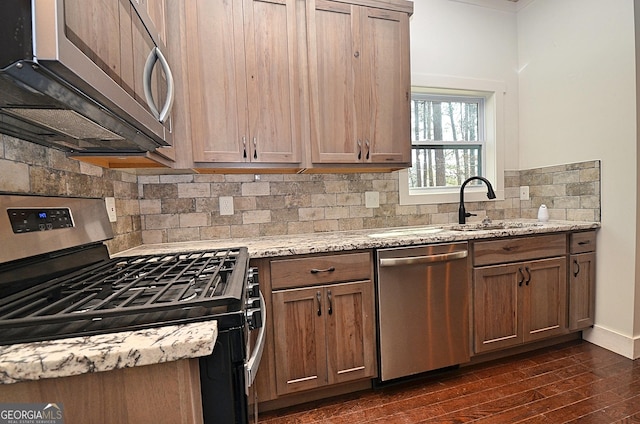 kitchen featuring light stone counters, a sink, appliances with stainless steel finishes, backsplash, and dark wood-style floors