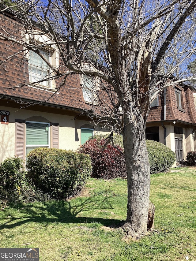 view of home's exterior featuring a yard, roof with shingles, mansard roof, and stucco siding