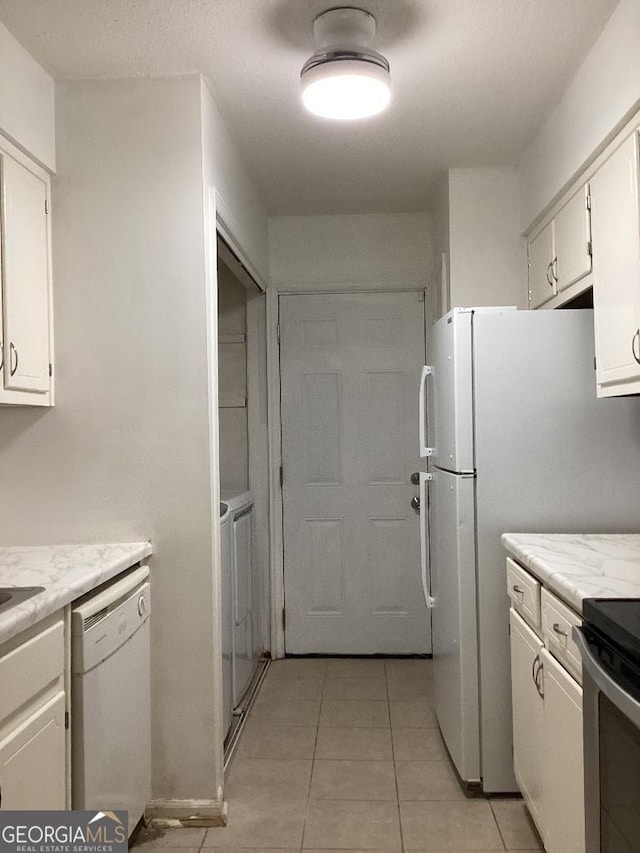 kitchen with light tile patterned floors, light stone counters, white appliances, and white cabinetry