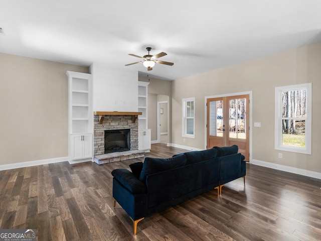 living area with a stone fireplace, baseboards, dark wood-type flooring, and french doors