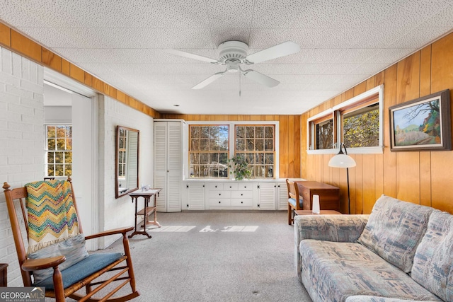 living room featuring a wealth of natural light, ceiling fan, wooden walls, and carpet flooring