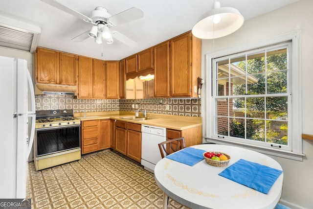 kitchen with under cabinet range hood, white appliances, a sink, light countertops, and tasteful backsplash