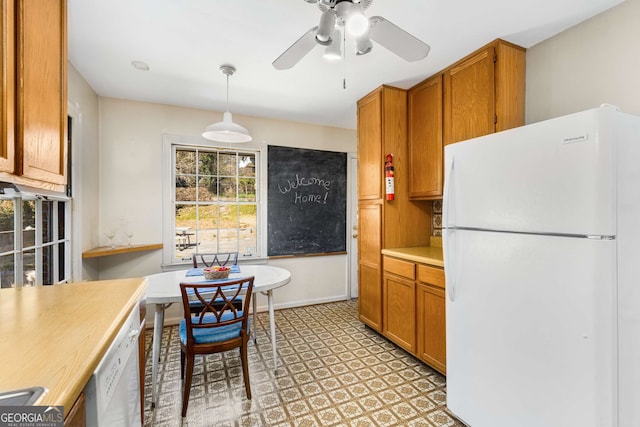 kitchen with pendant lighting, light countertops, brown cabinetry, a ceiling fan, and white appliances