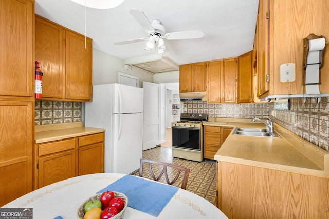 kitchen featuring under cabinet range hood, a sink, range with gas stovetop, light countertops, and freestanding refrigerator