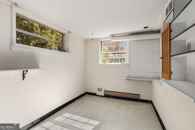 unfurnished room featuring a baseboard radiator, a textured ceiling, a wealth of natural light, and tile patterned floors