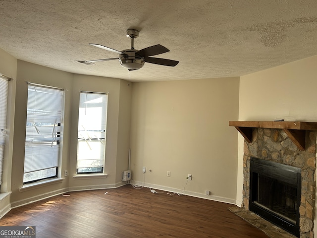 unfurnished living room with baseboards, ceiling fan, dark wood-style flooring, a textured ceiling, and a fireplace