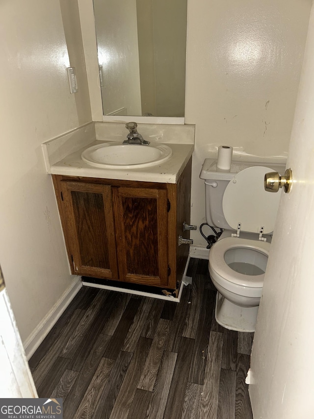 half bathroom featuring baseboards, vanity, toilet, and wood finished floors