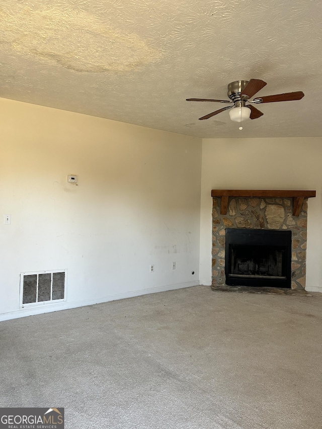 unfurnished living room with a textured ceiling, carpet floors, a stone fireplace, and visible vents