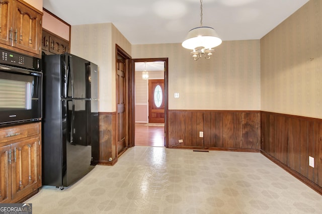 kitchen featuring a wainscoted wall, hanging light fixtures, black appliances, and wallpapered walls