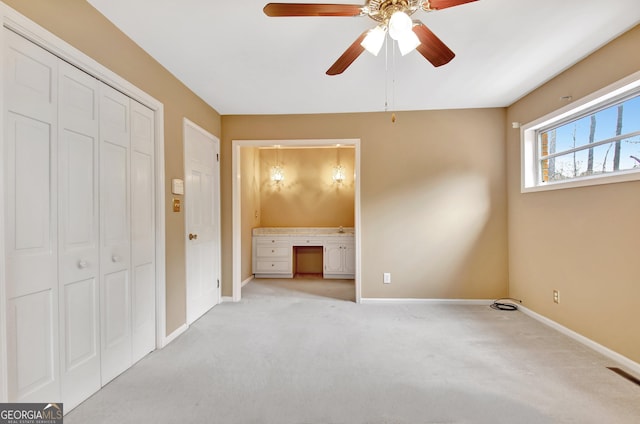 unfurnished bedroom with built in desk, a closet, light colored carpet, ensuite bath, and baseboards