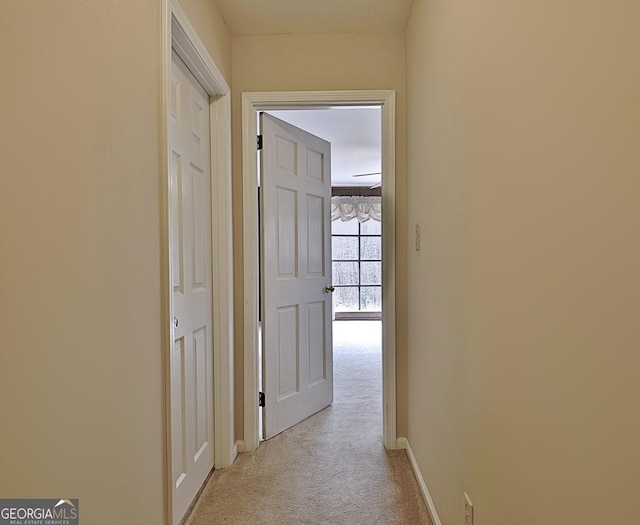 hallway featuring light carpet and baseboards