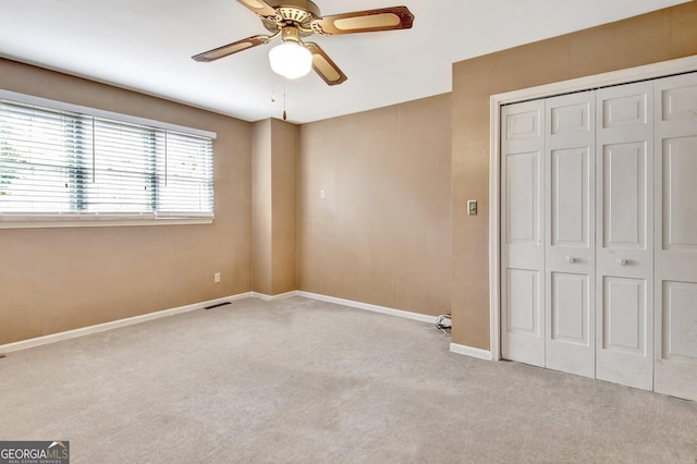 unfurnished bedroom featuring ceiling fan, light colored carpet, visible vents, baseboards, and a closet