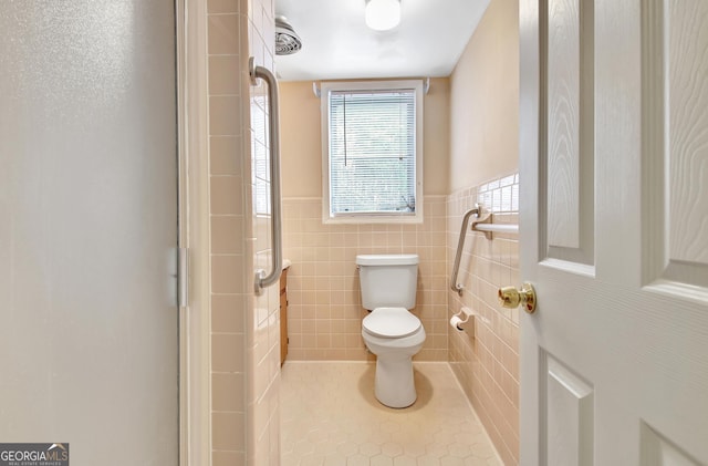 bathroom featuring toilet, a wainscoted wall, tile patterned flooring, and tile walls