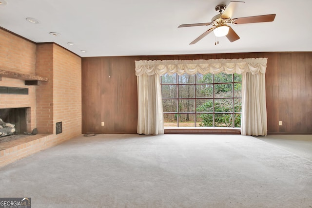 unfurnished living room featuring light colored carpet, a fireplace, wood walls, and visible vents