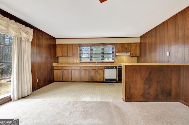 kitchen featuring under cabinet range hood, light countertops, dishwasher, and wood walls